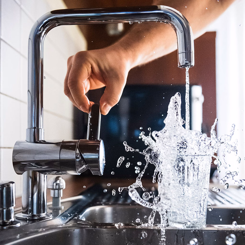 Wasser fließt explosiv aus einem Wasserhahn in ein Glas
