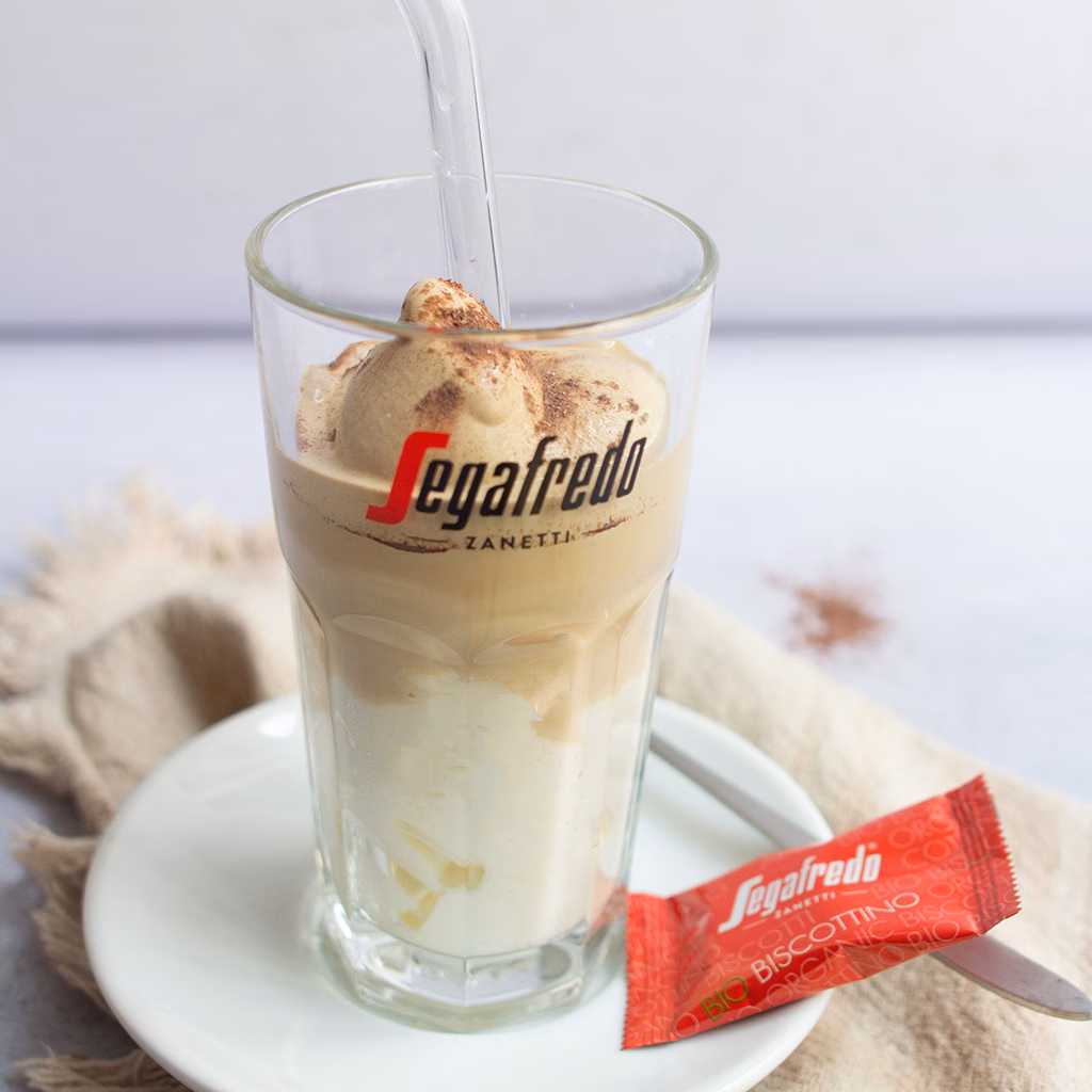 Imagebild Latte Macchiato-Glas mit Schlagobers und Kaffeeeis und einer Keksverpackung